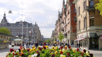Längst fram syns en stor kruka med blommor på en gata. Bakom syns resten av gatan och flera gamla hus.