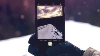 En person håller en mobil i ett snötäckt landskap