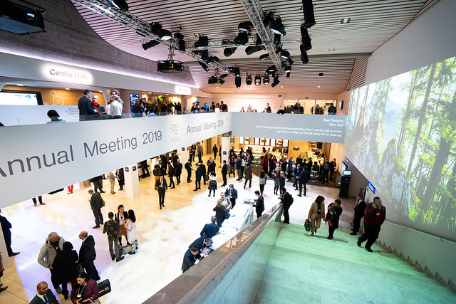 Många människor står utsprida i en stor foajé. Några står på en balkong över de andra. På balkongens sida står det "Annual meeting 2019".