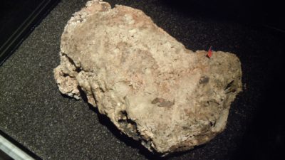 En stor klump ligger på ett svart underlag. I klumpen syns vita prickar och i ena hörnet sticker det ut ett godispapper.