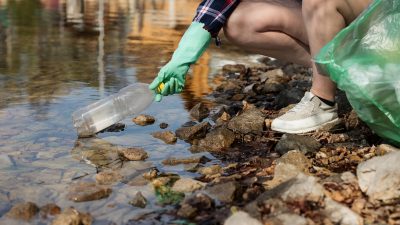 En person plockar upp plastskräp från naturen.