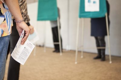 Människor röstar bakom valskärmar.